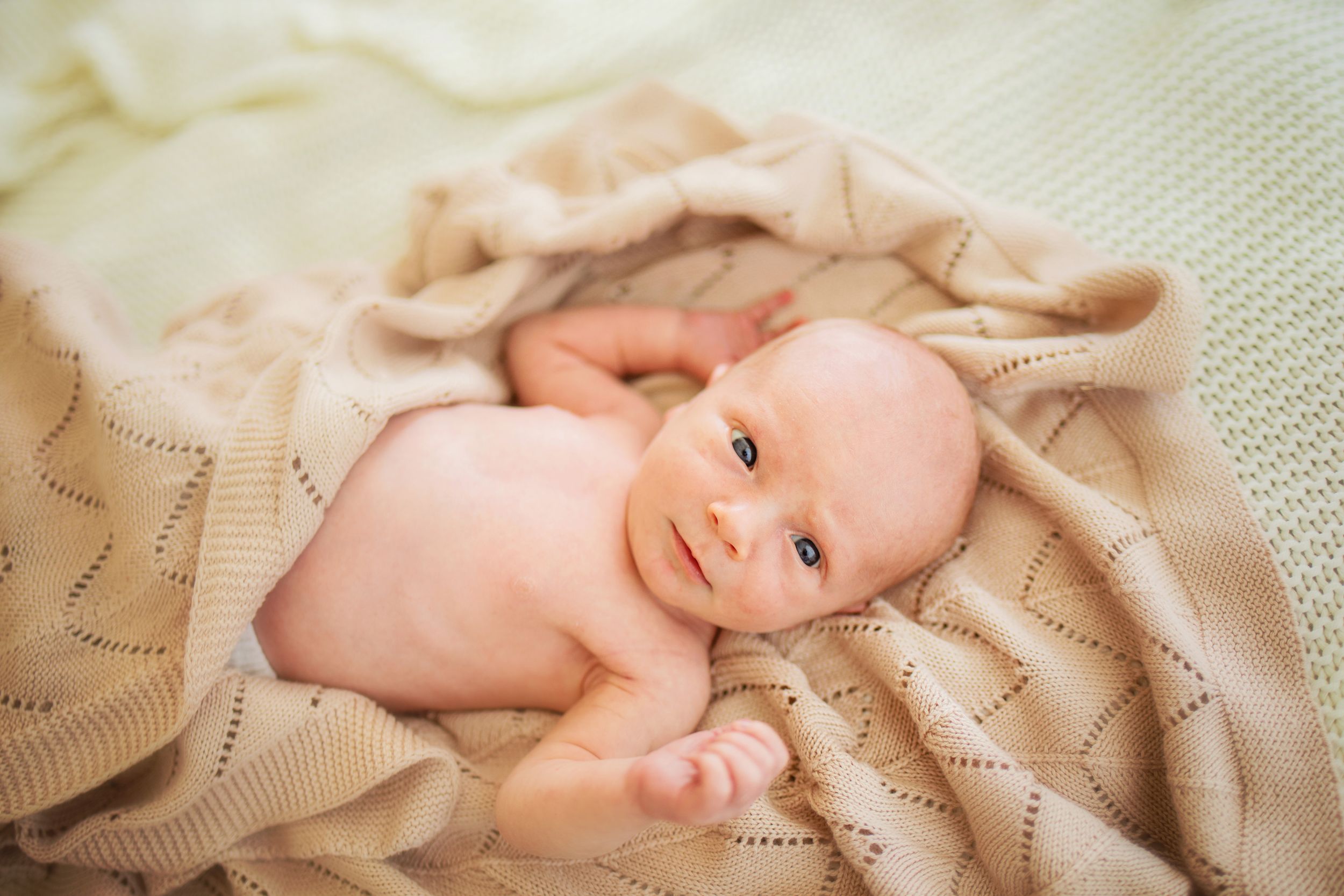 A baby lies on soft beige fabric while looking up with a gentle expression.