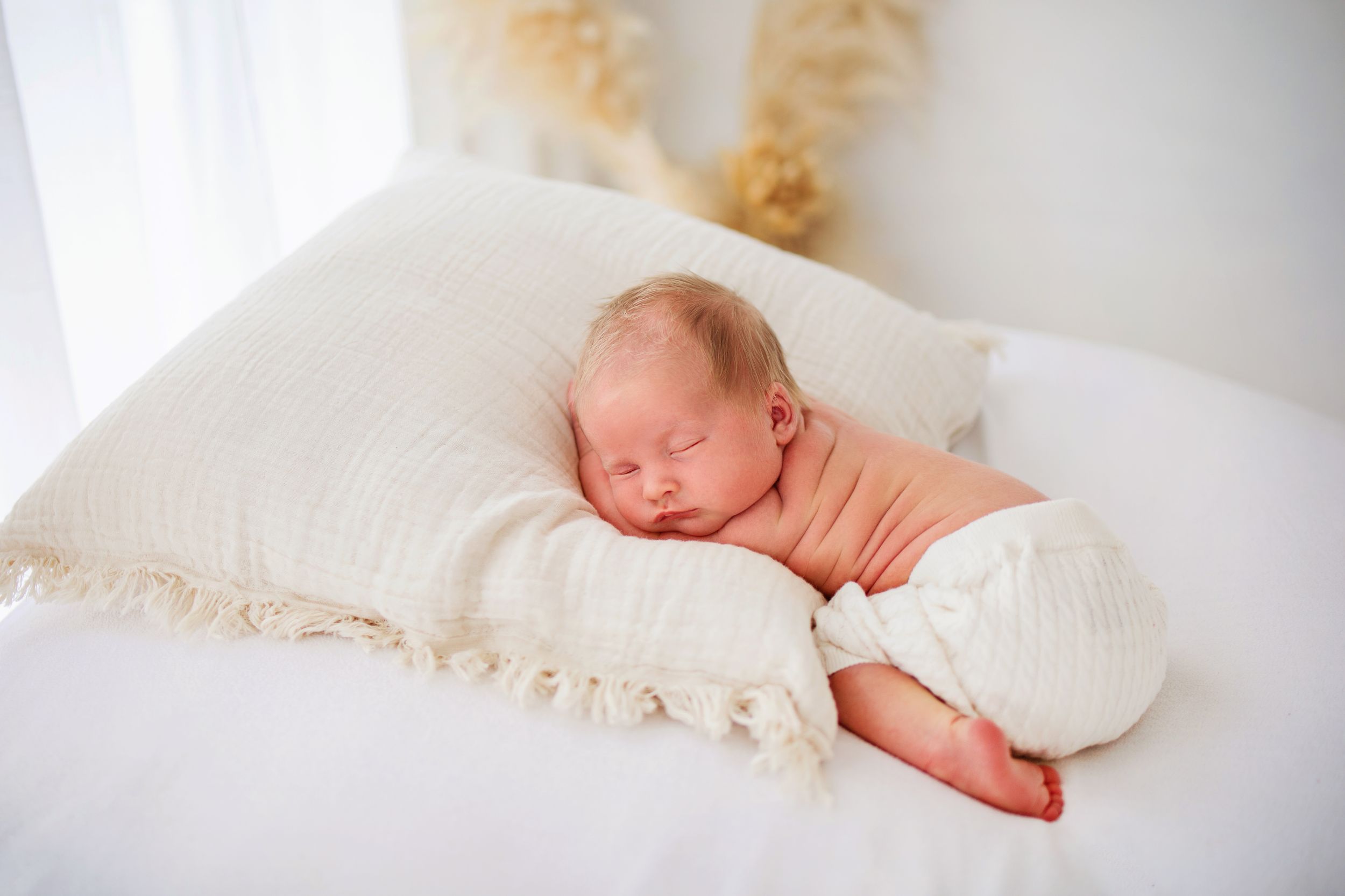 A newborn baby sleeping peacefully on a white pillow with ruffled edges.