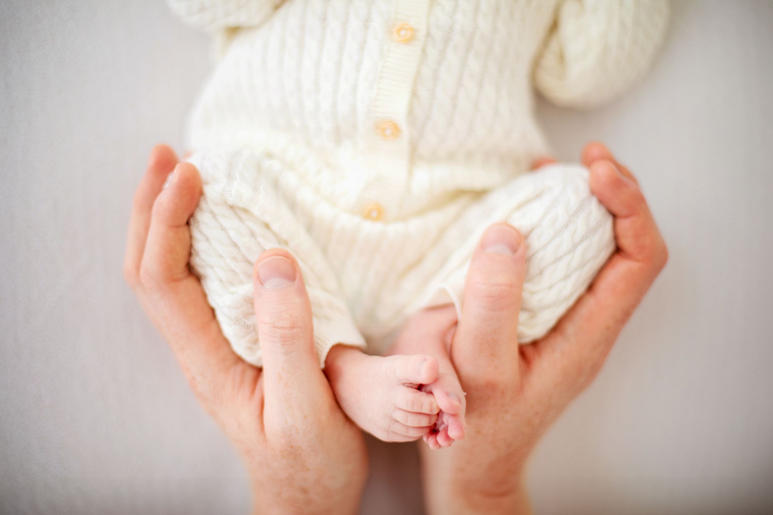 Close-up photo series showing hands gently holding a sleeping newborn baby in a white wrap.