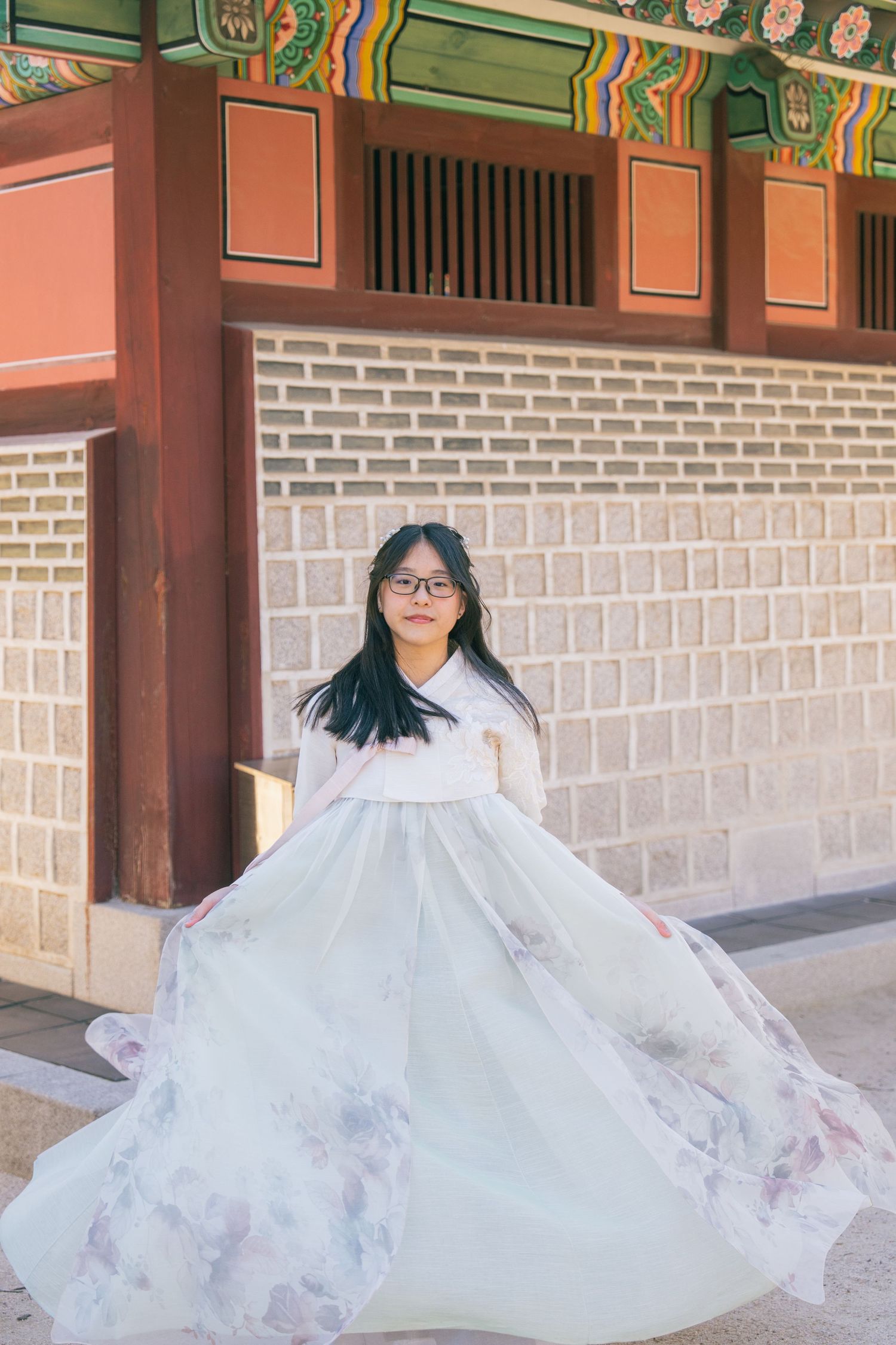 A person in a flowing white dress twirls gracefully under traditional Korean architecture at a historic temple.