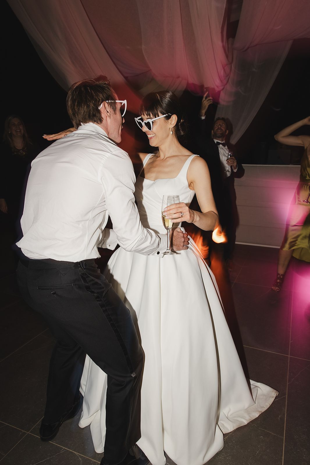 Bride and groom sharing fun moment on the dancefloor with sunglasses.