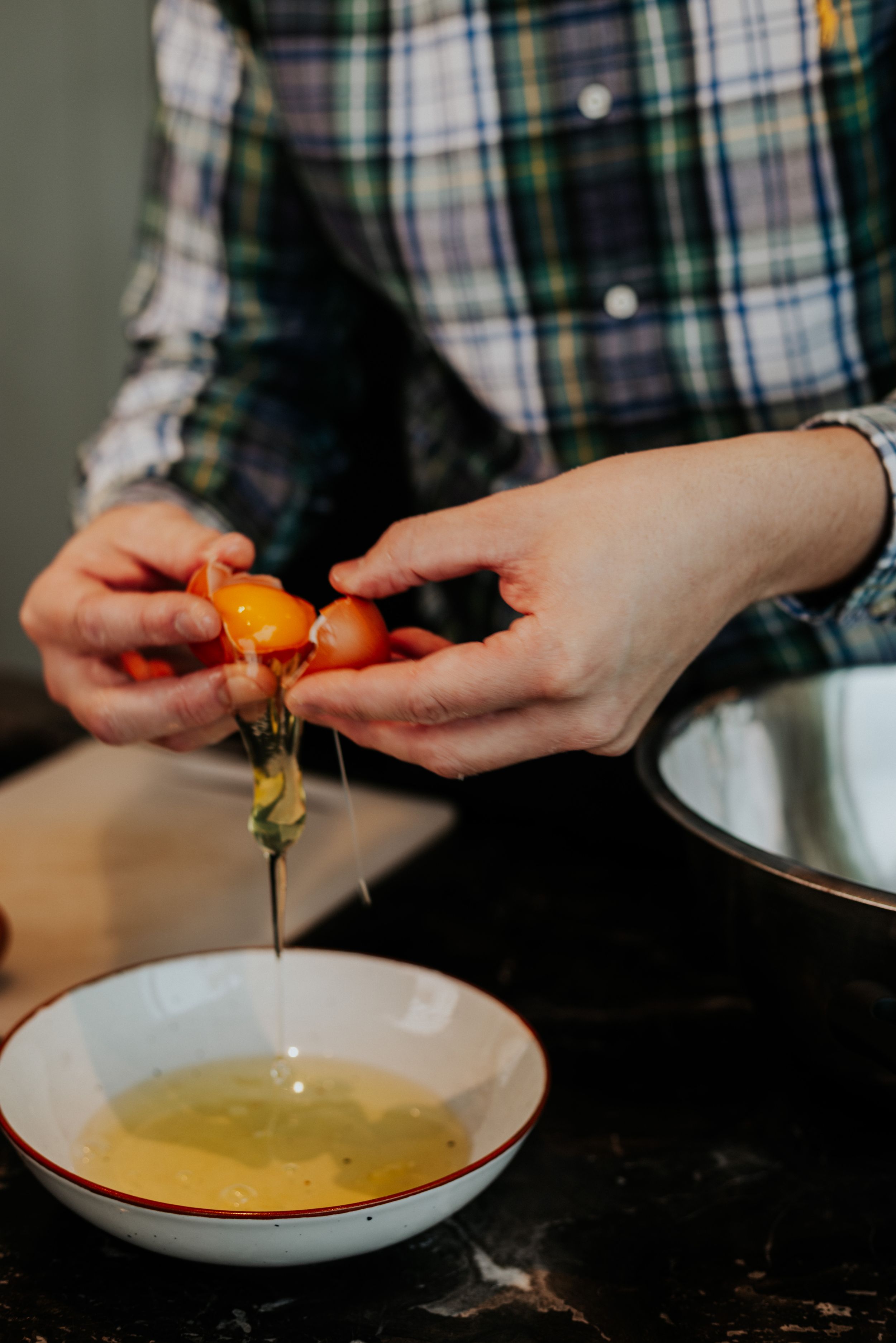 Cracking fresh eggs into bowl of clear liquid on dark counter.