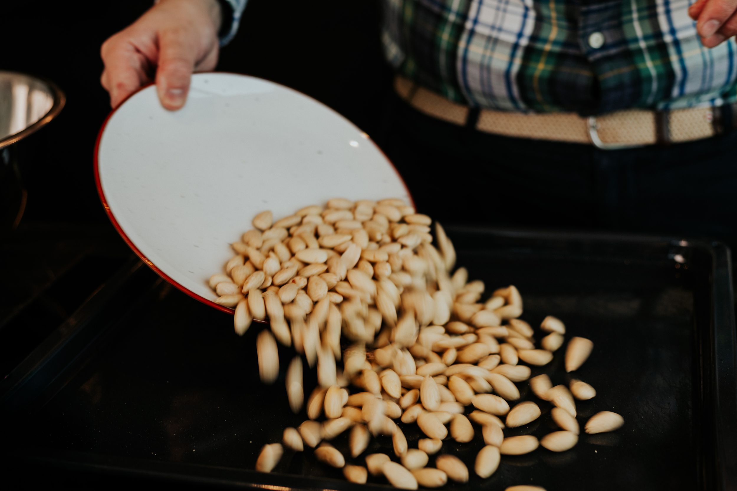 Pouring white nuts or beans from plate into dark baking pan.
