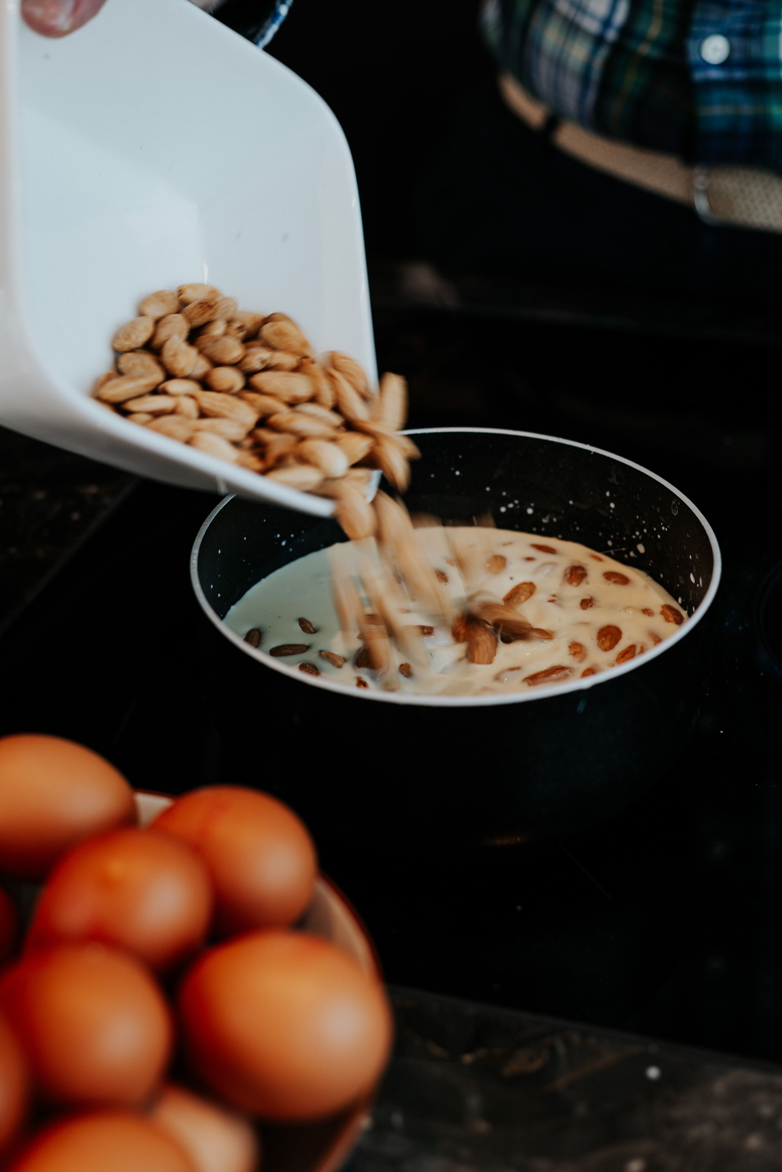 Pouring almonds into mixing bowl with brown liquid and fresh eggs nearby.