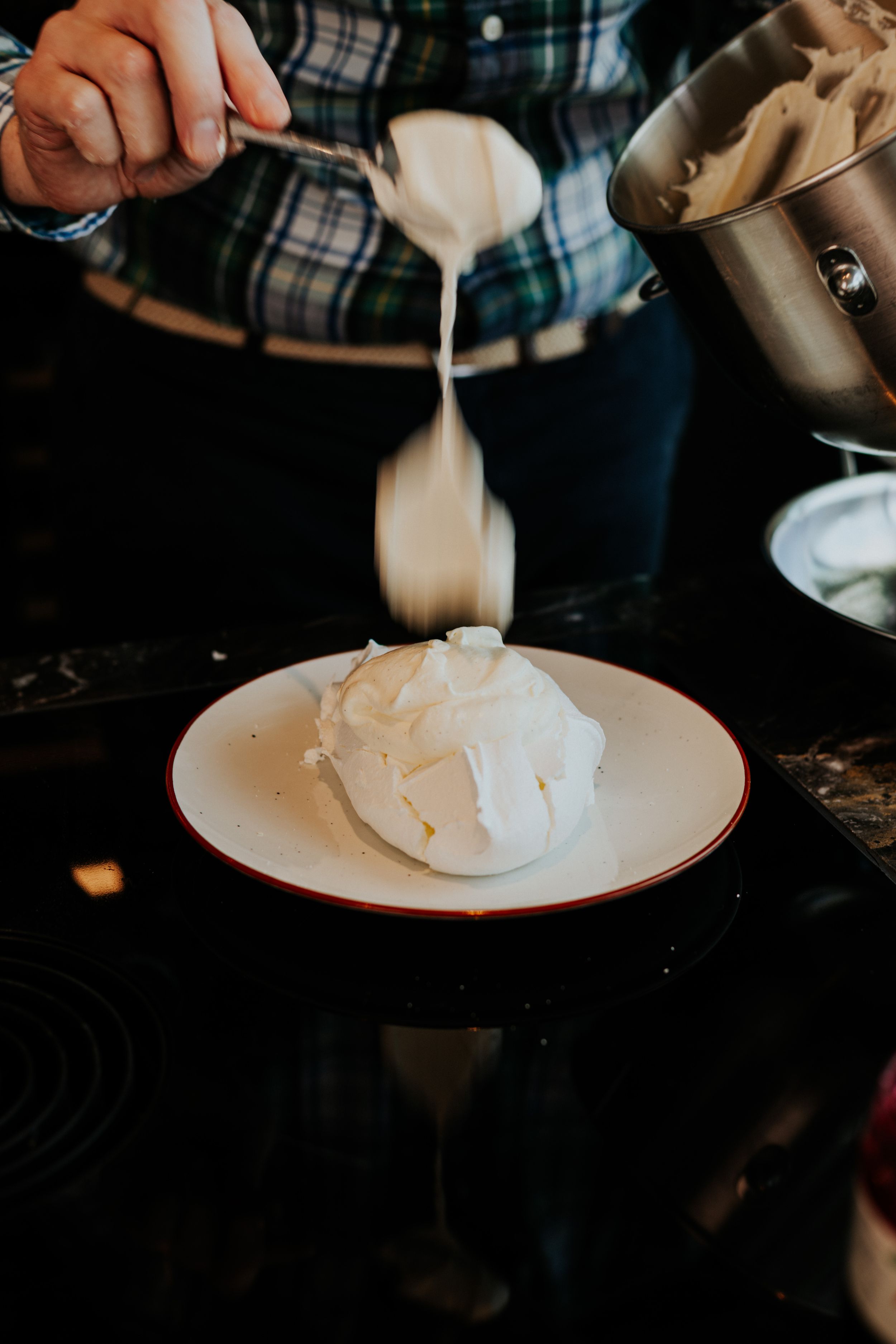 Pouring white liquid onto whipped cream or meringue on plate.