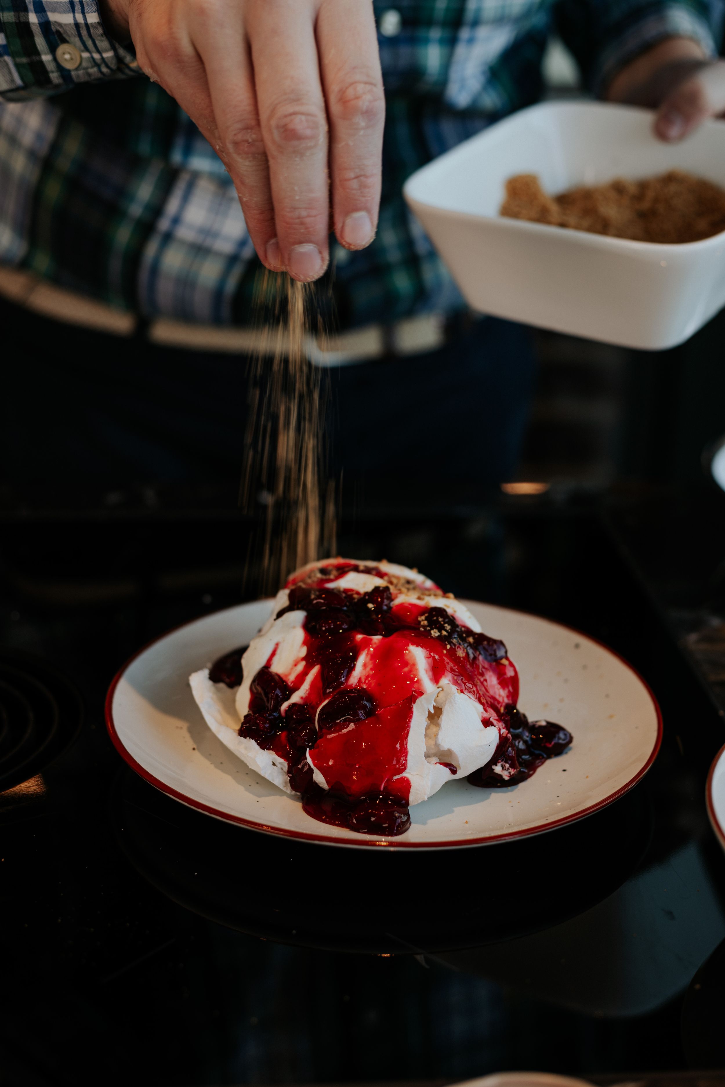 A dessert plate with red sauce and whipped cream being garnished with a sprinkle topping.