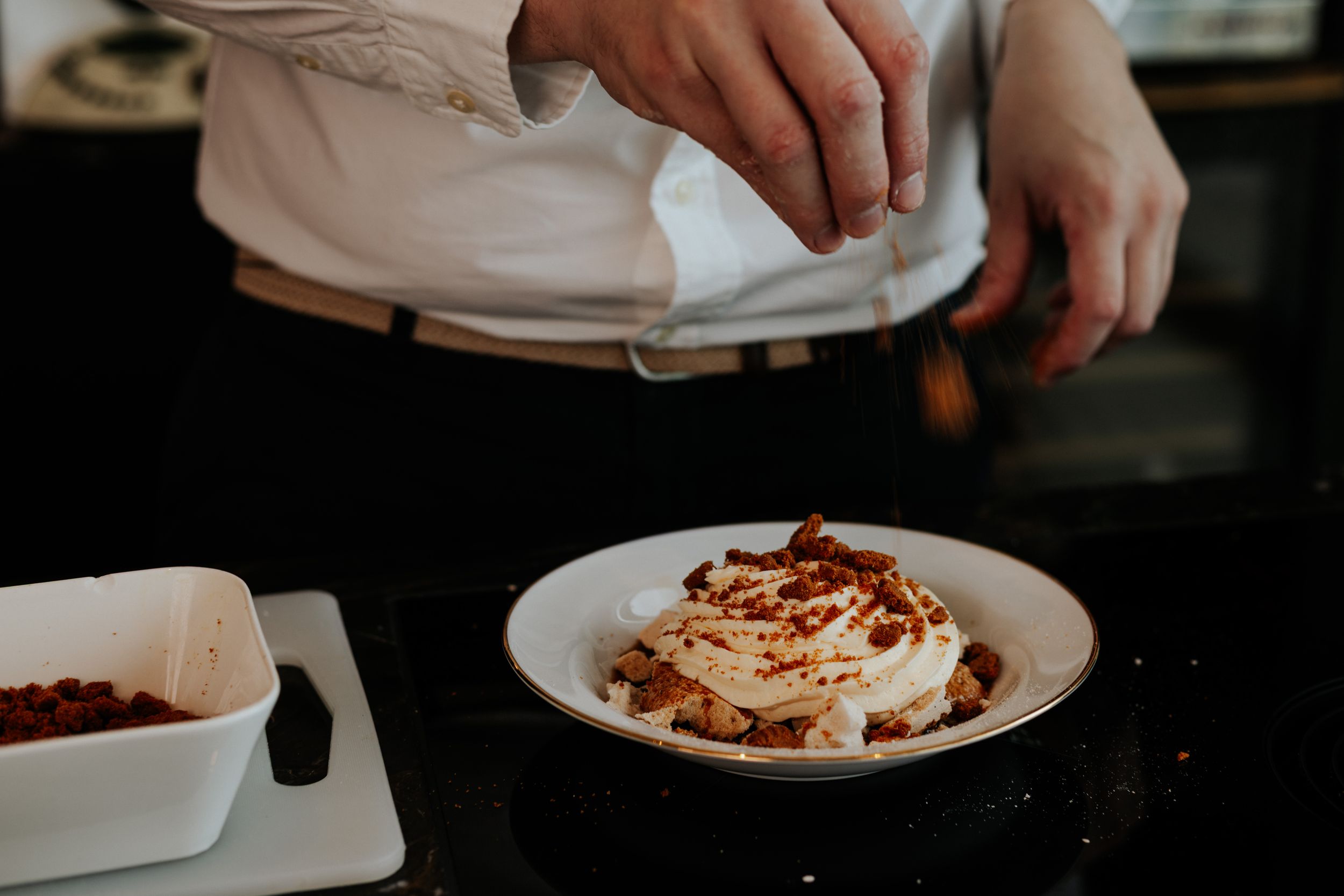A series of hands garnishing plates of food with toppings in a restaurant setting.
