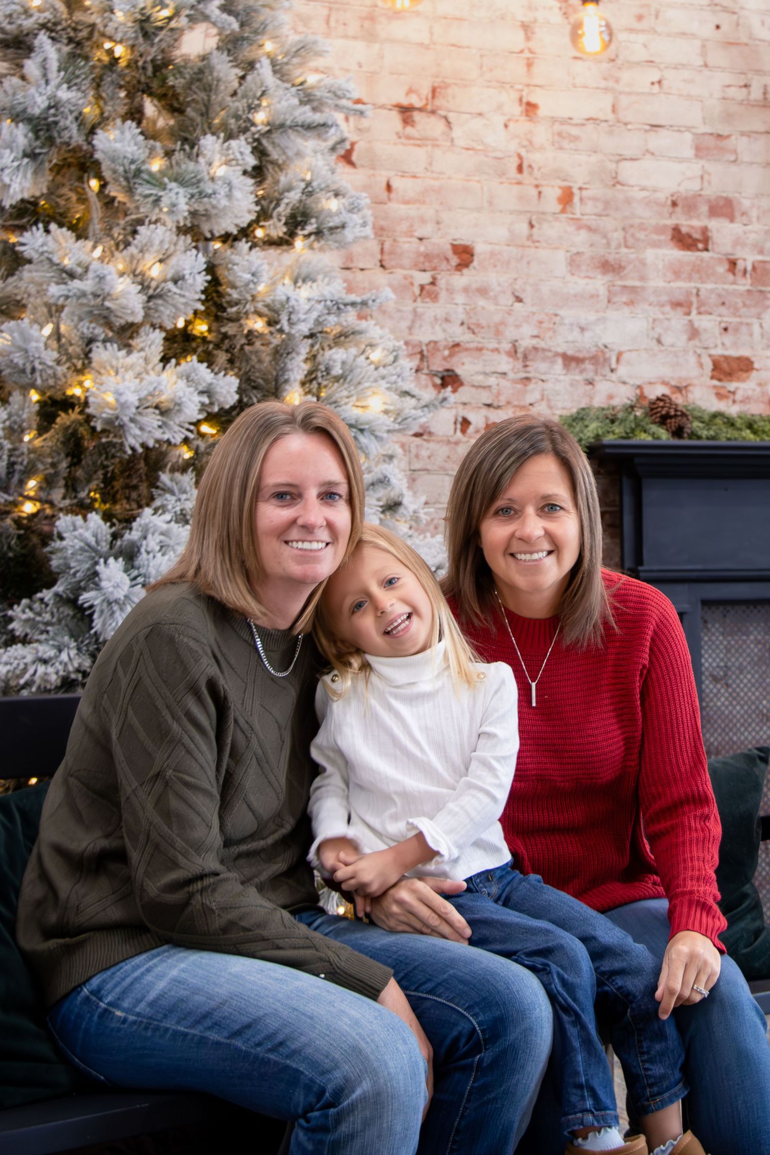 Two mom family cuddling their daughter during a Cincinnati Christmas photo session with soft holiday decor and warm studio lighting