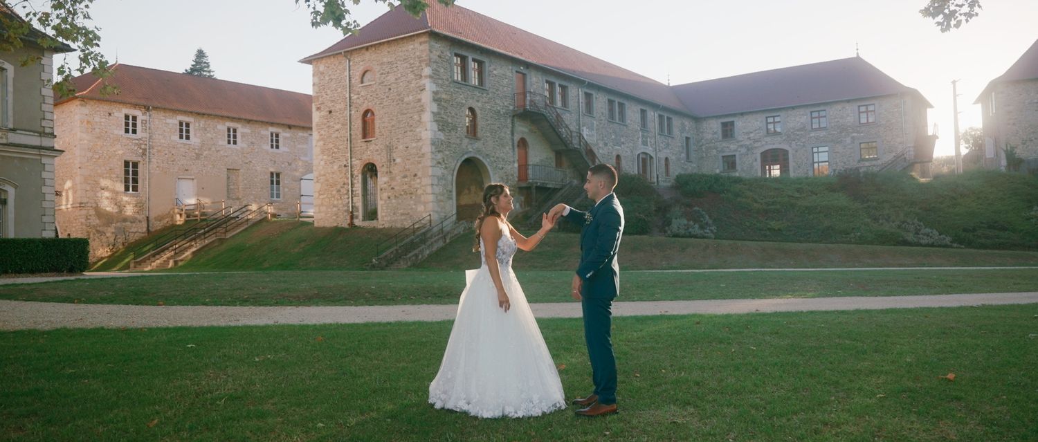 A couple stands together outside a historic stone castle building during their wedding celebration.