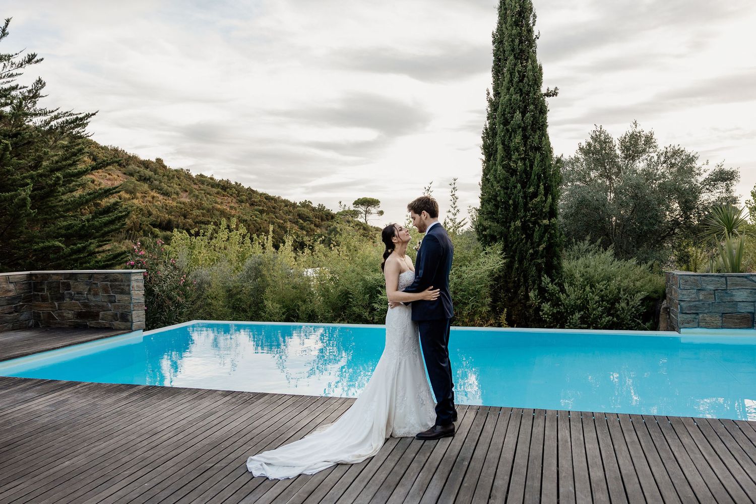A panoramic view of a wedding venue in Tuscany with cypress trees, a pool, and a wooden deck against a scenic landscape.