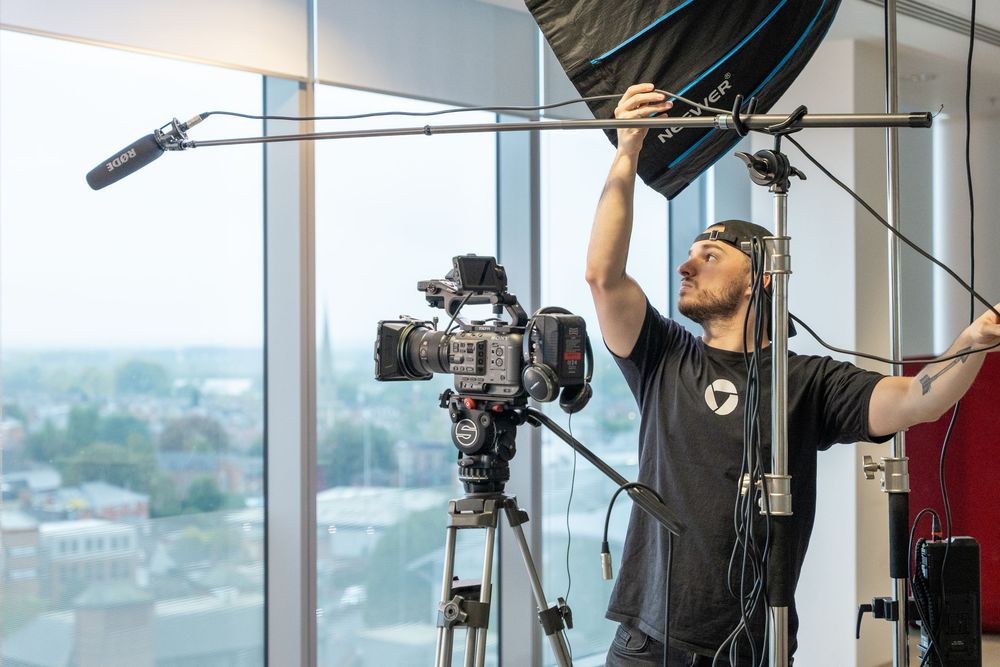 Production crew adjusting camera and lighting gear during commercial video shoot in windowed office setting.