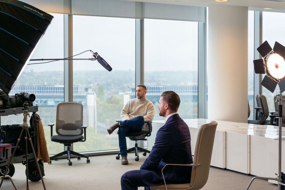 Professional film crew setting up camera equipment in a bright office space with large windows.