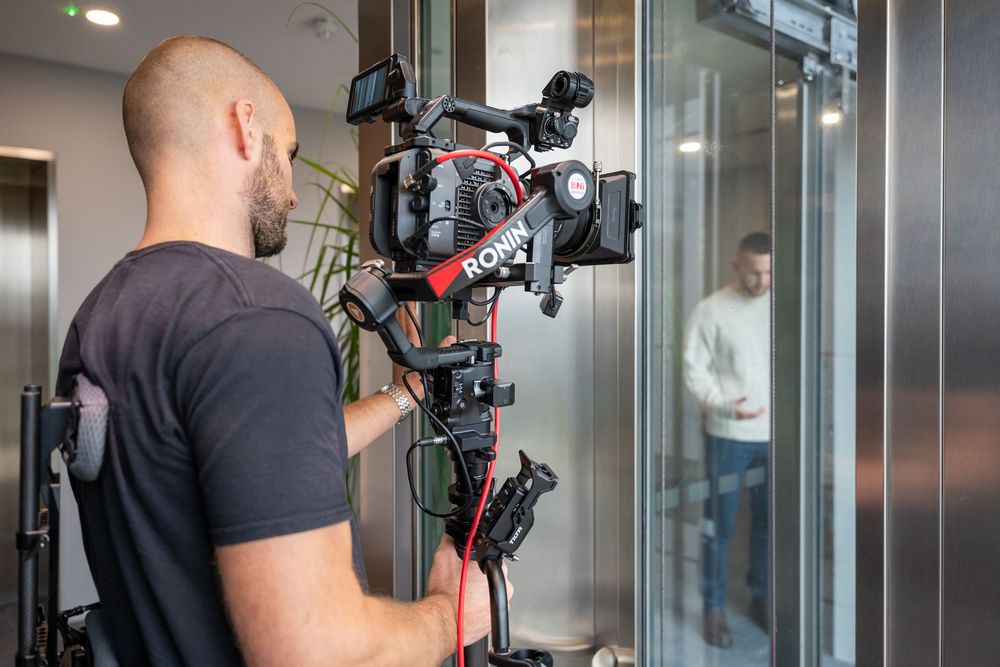 Camera operator films with stabilized equipment in sleek office hallway.