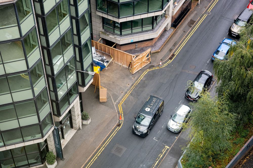 Aerial view of a modern apartment building with green balconies and parked cars on the street below.