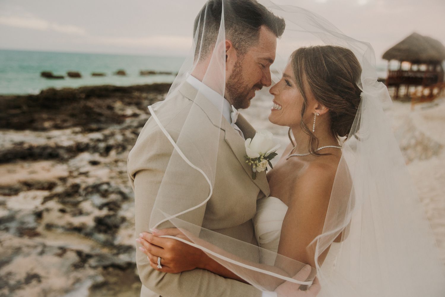 A romantic beach wedding photoshoot with the couple embracing on a sandy tropical shore at sunset. El Dorado Royale Wedding Photographer