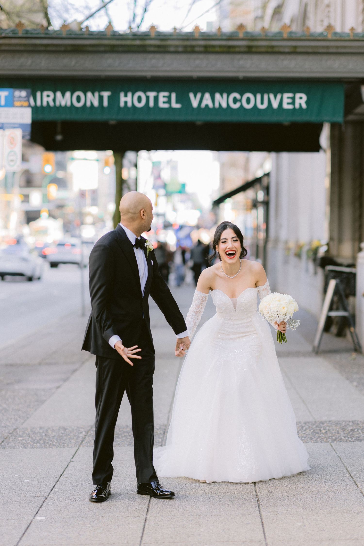 A playful wedding couple shares candid moments in front of the Fairmont Hotel Vancouver.