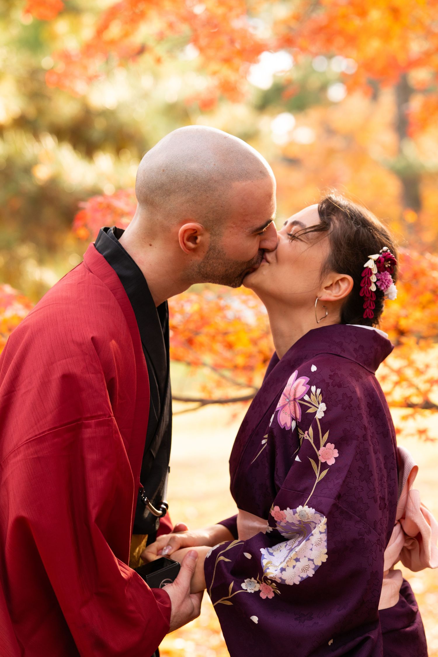 Couple in traditional Japanese kimono sharing a kiss surrounded by brilliant orange autumn leaves.