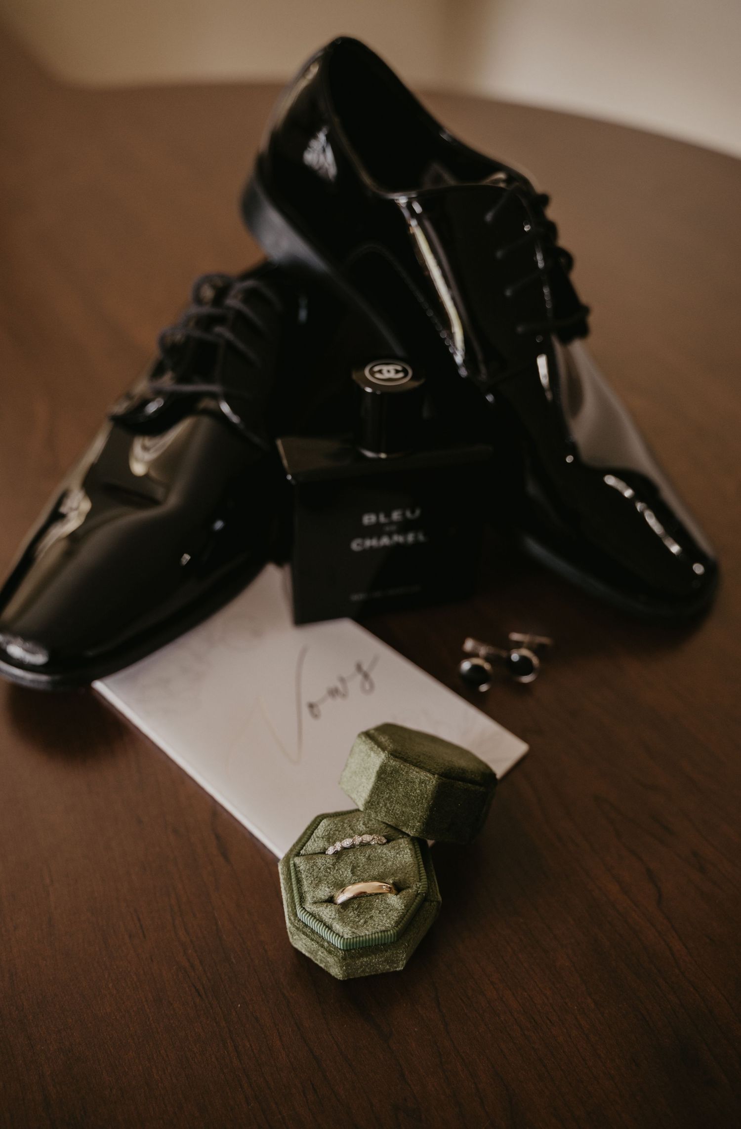 Black dress shoes and wedding rings displayed on a dark wooden surface.