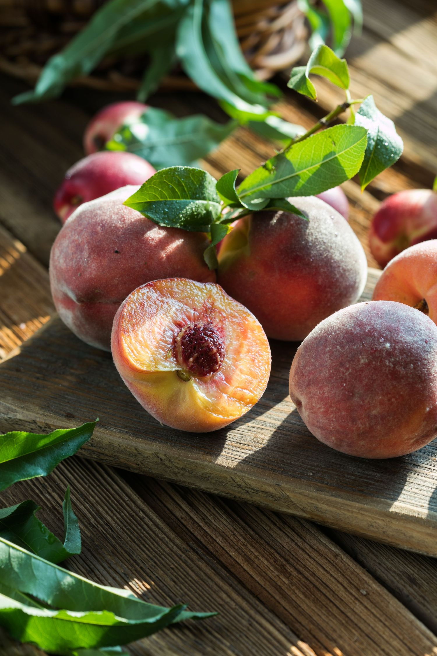 Fresh ripe peaches with green leaves arranged on rustic wooden surface in warm sunlight.