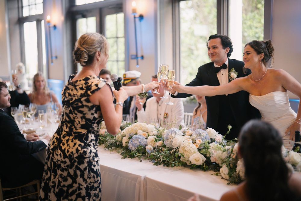Wedding reception tables decorated with elegant floral centerpieces and white linens in a bright venue.