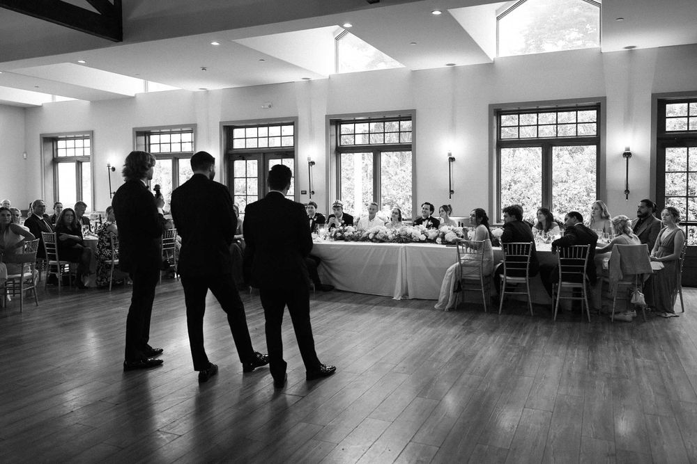 Black and white panoramic view of a spacious wedding reception venue with guests seated at tables.