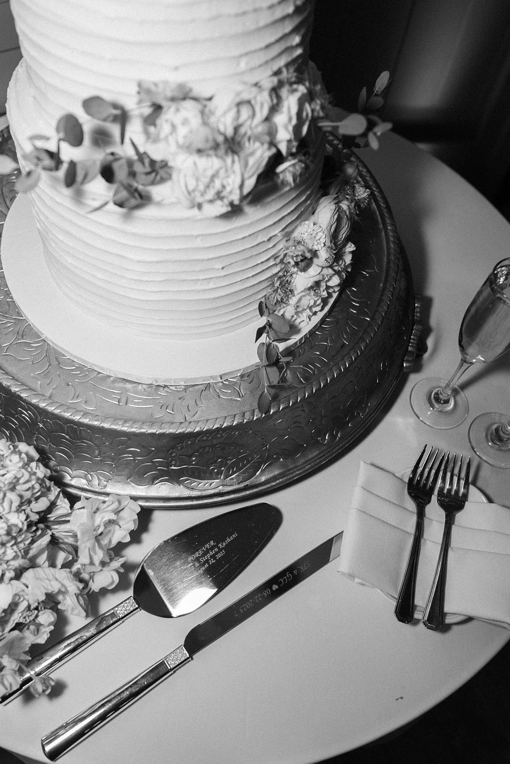 A black and white close-up series of a wedding cake being cut with a silver knife on a white surface.