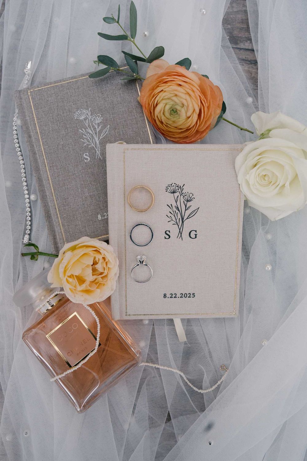 Elegant wedding stationery and floral details with orange ranunculus and white roses on soft tulle fabric.