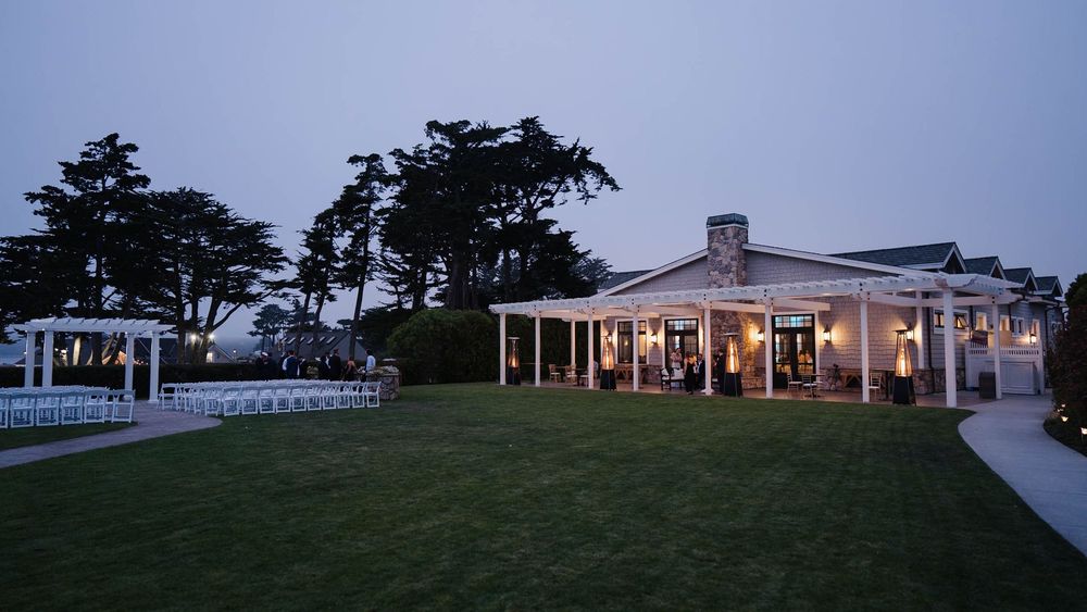 An elegant wedding venue with white columns and porch lights glowing at dusk beside a manicured lawn.