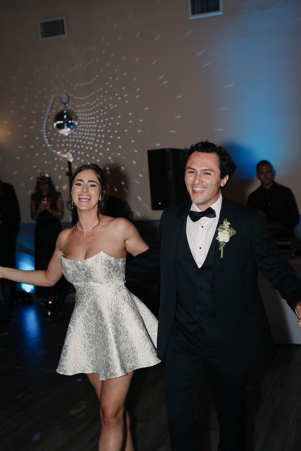 A couple dances joyfully at their wedding reception under blue lighting and disco effects.
