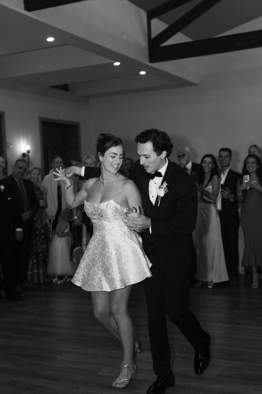 A couple performs a romantic dip dance move on a wooden dance floor at a wedding reception.