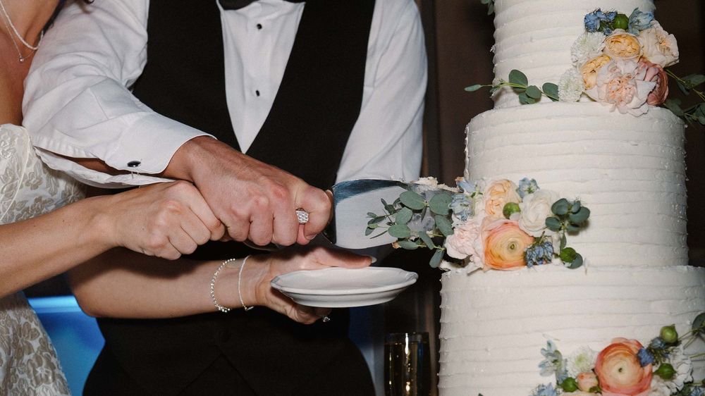 A sequence of hands cutting and serving slices of an elegant white wedding cake decorated with peach flowers.