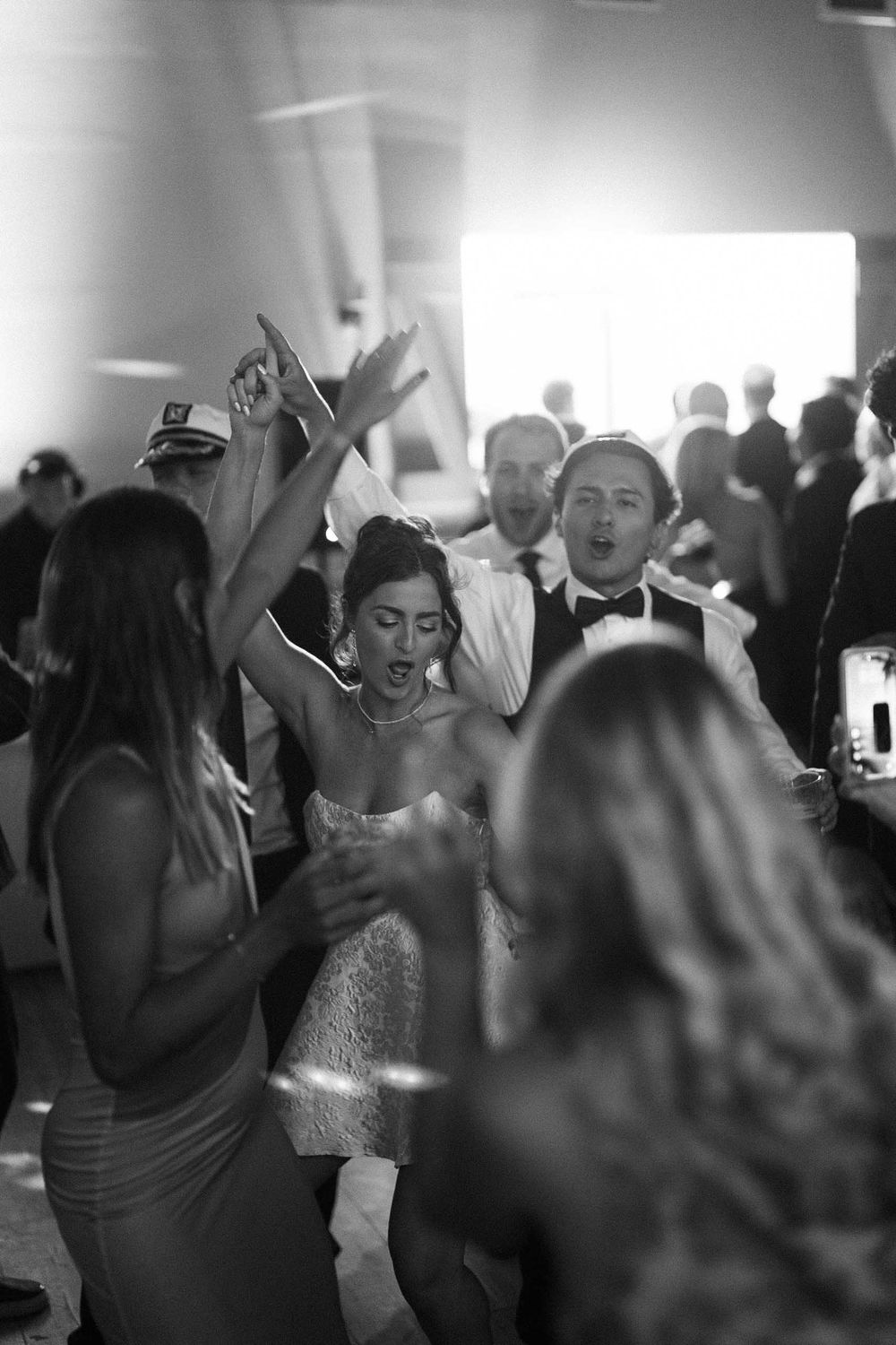Wedding guests dance and celebrate energetically on a crowded dance floor at a reception party.