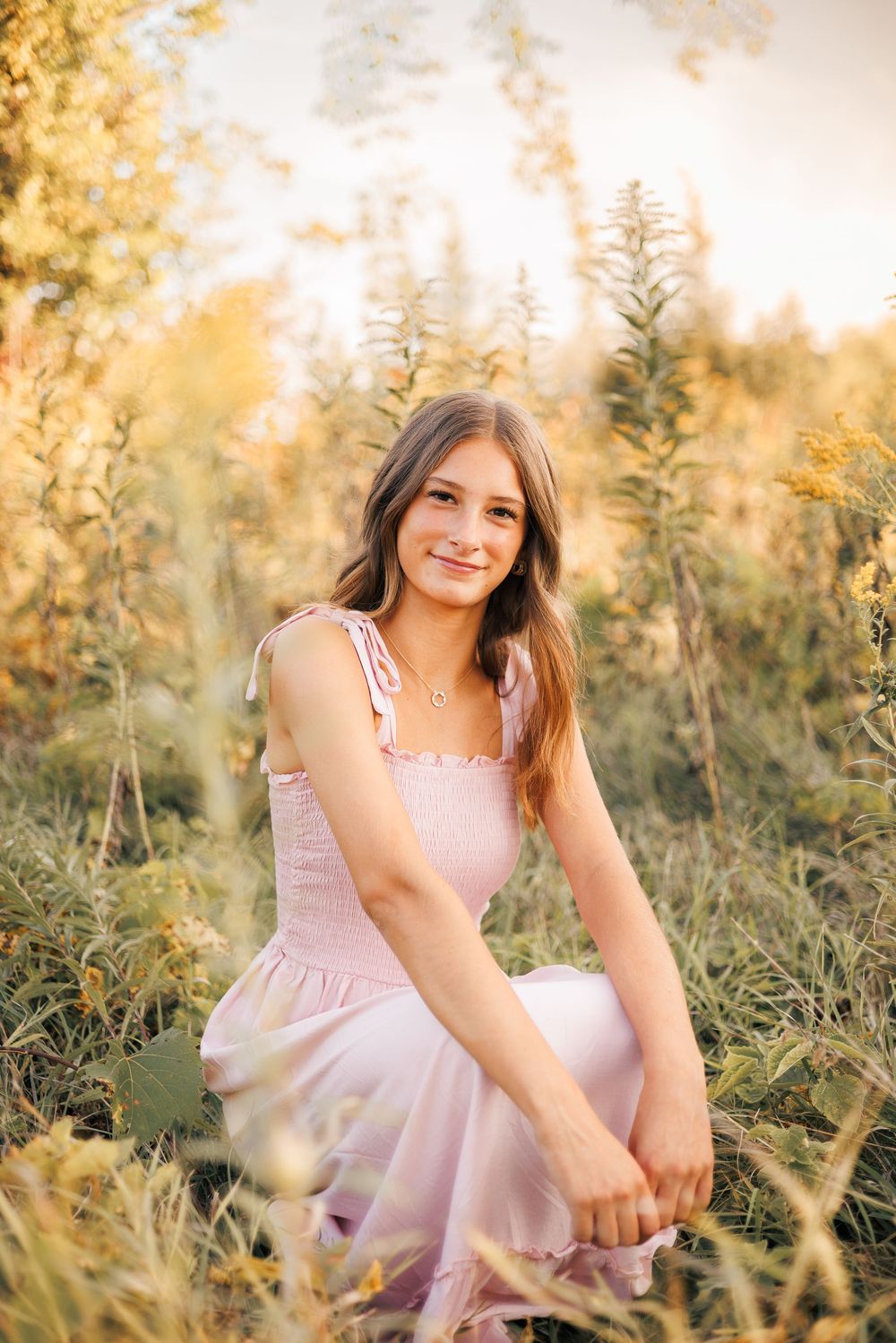 A person in a pink dress sits among wildflowers during golden hour in a dreamy outdoor setting.