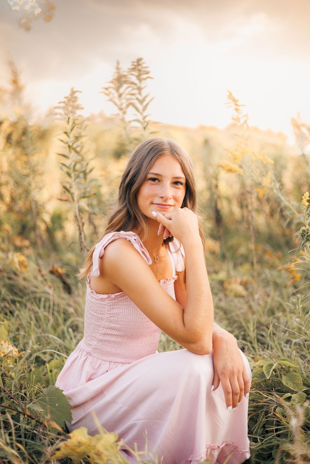 A soft pink dress stands out against tall wildflowers and grass during golden hour sunset lighting in a meadow.