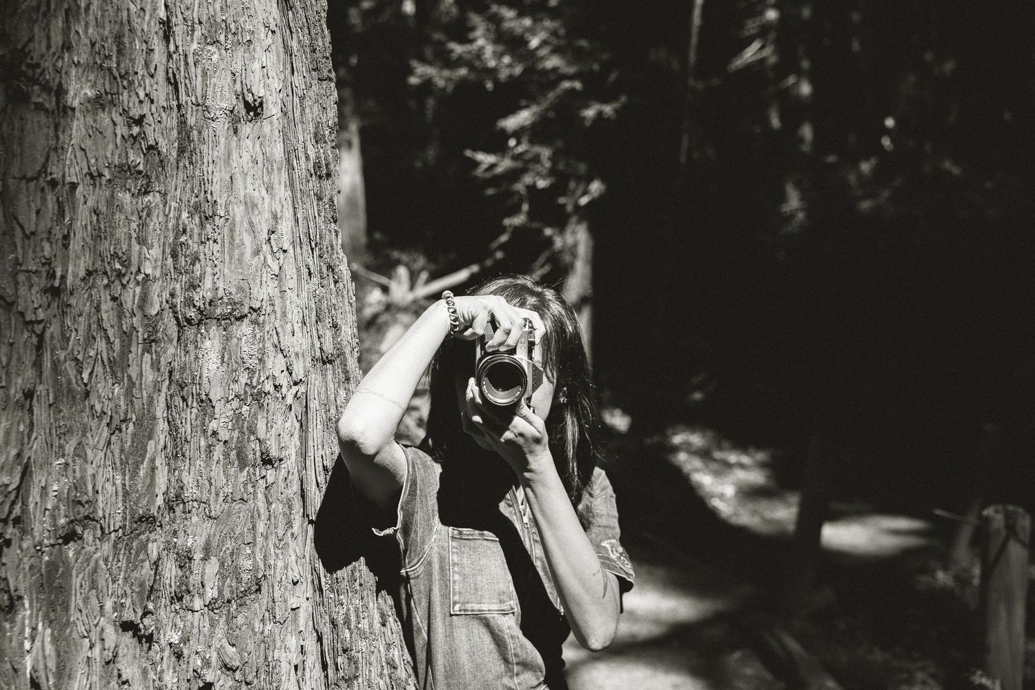 Black and white photograph showing someone hiding behind a tree trunk in a playful game of hide and seek.