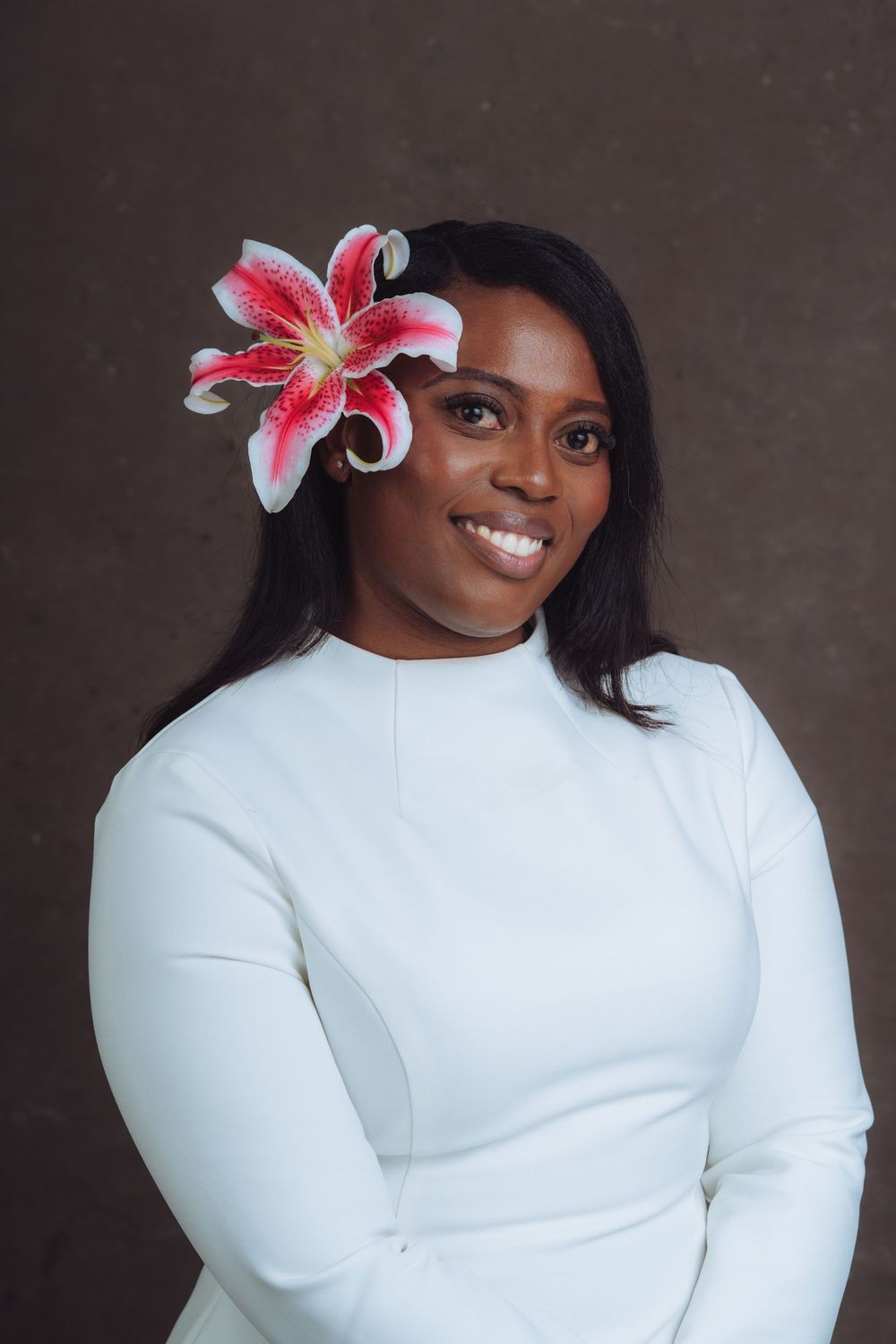 Studio portrait with pink lily hair accessory and white top against brown backdrop.