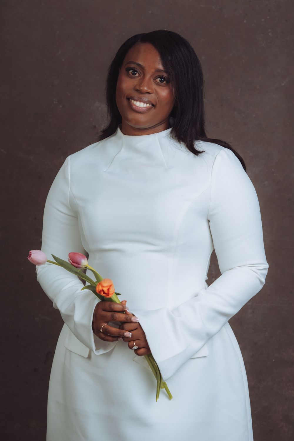 Elegant pose with tulip flowers against dark backdrop wearing crisp white sweater.