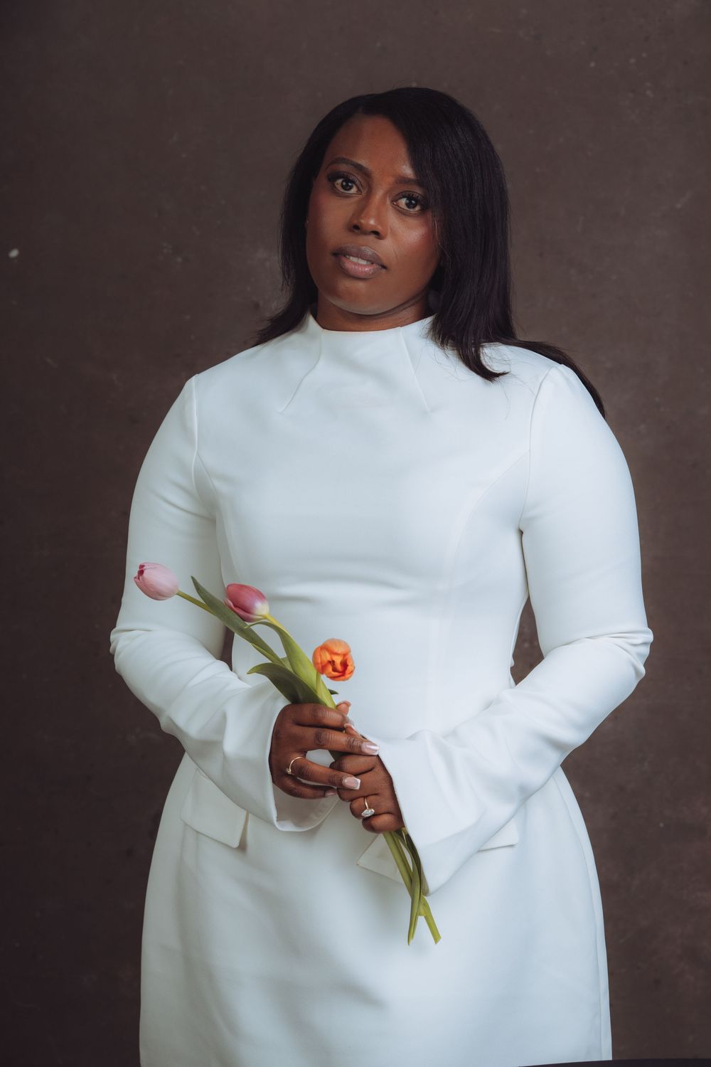 Fashion portrait holding colorful tulips while wearing white sweater against textured backdrop.