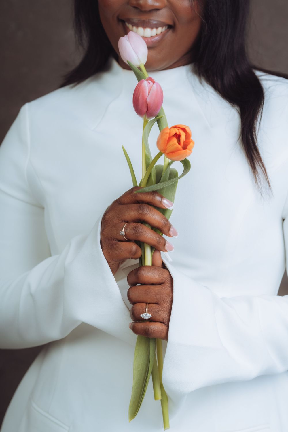 Close-up shot holding pink and orange tulips against white sweater and dark background.