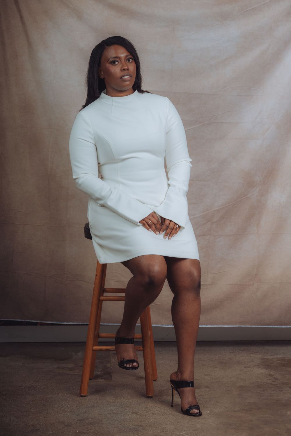 Modern fashion portrait on wooden stool wearing white sweater dress and black sandals.