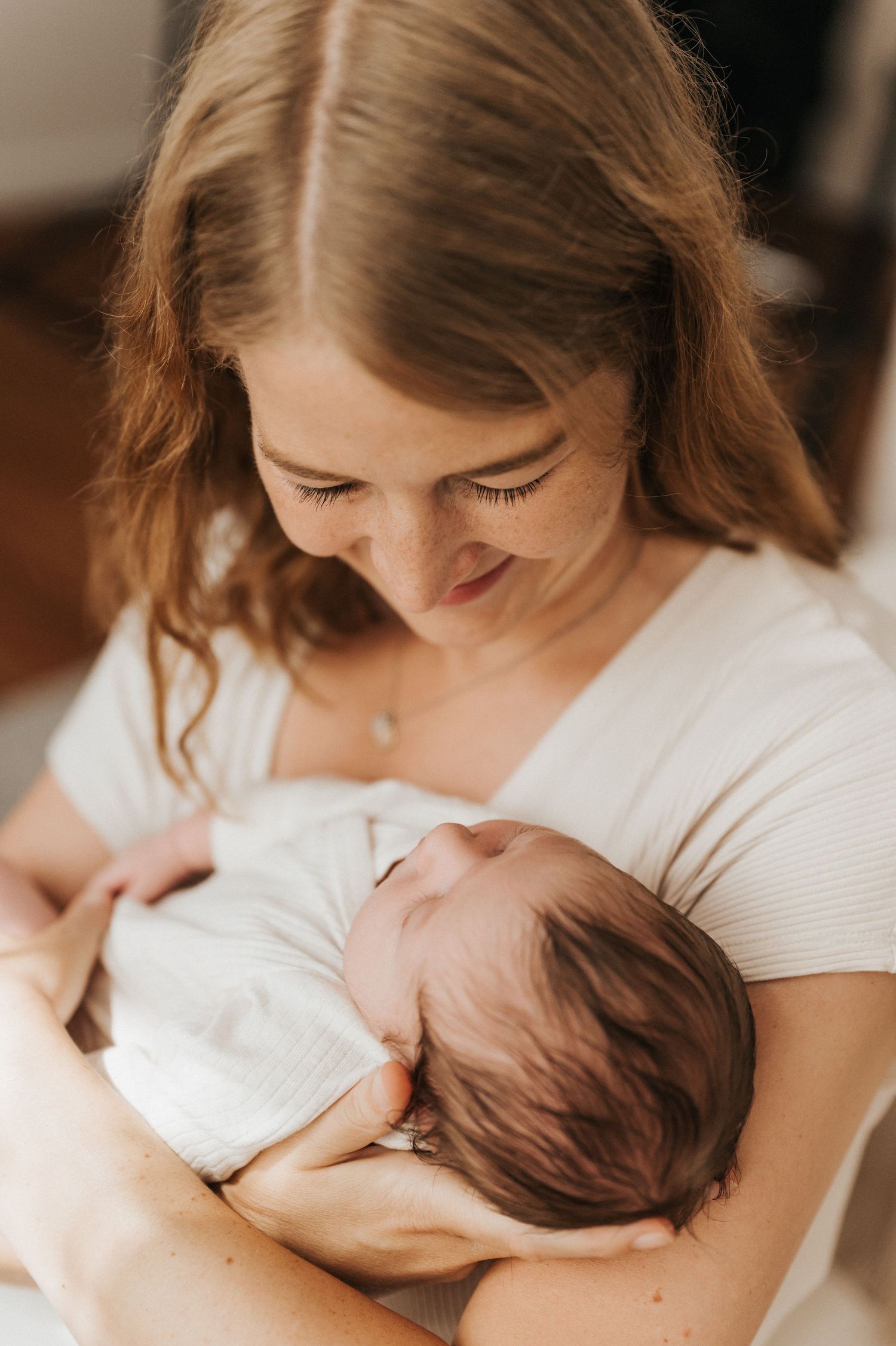 A mother in a white top cradles and breastfeeds her newborn baby in a series of intimate nursing photos.