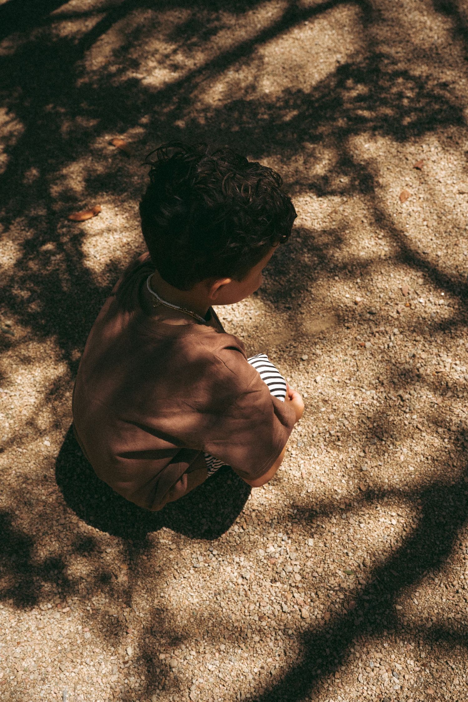 Artistic overhead shot of a child sitting in dappled sunlight and shadows.