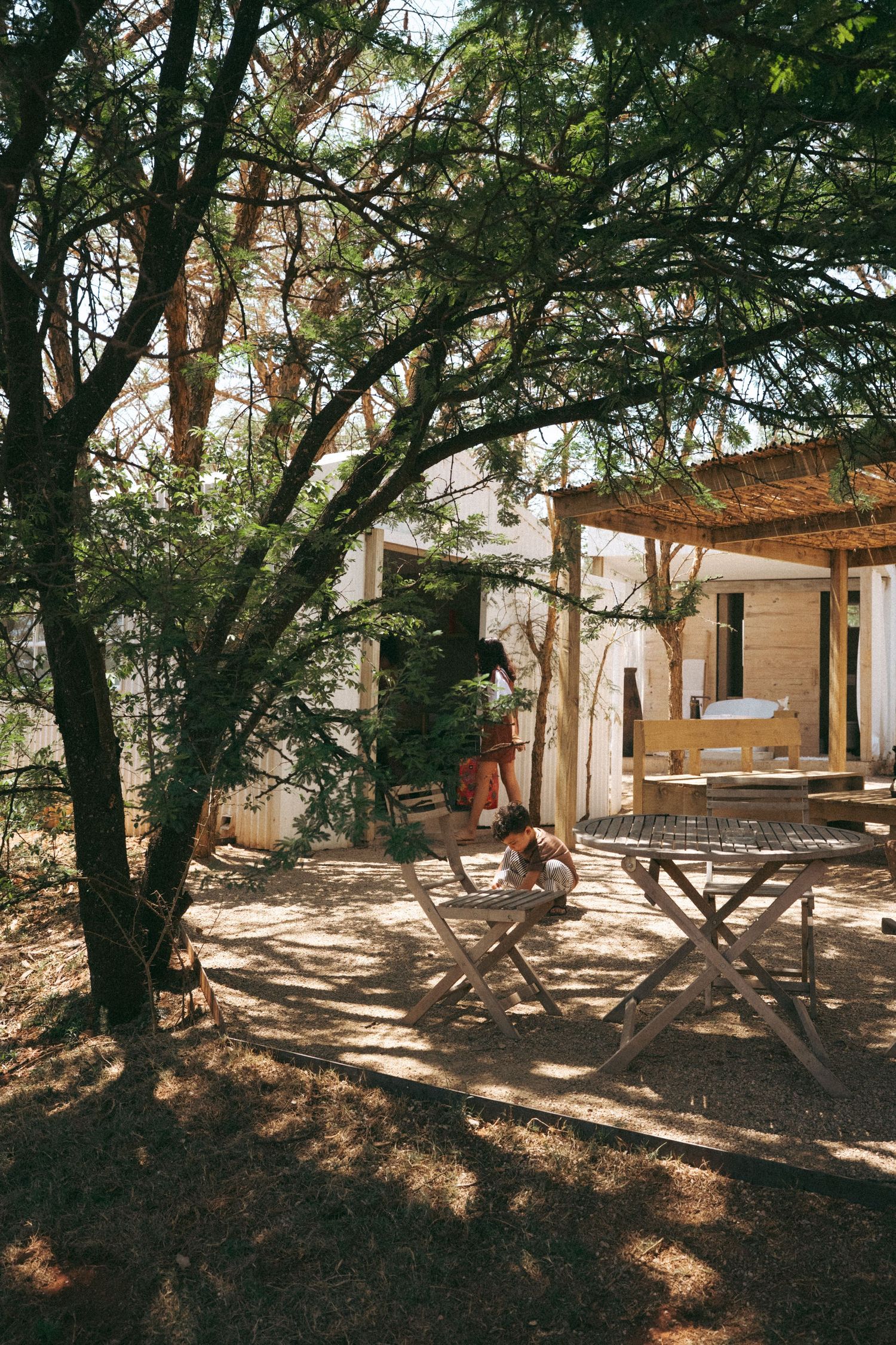 Peaceful outdoor seating area with wooden furniture under large shady trees.