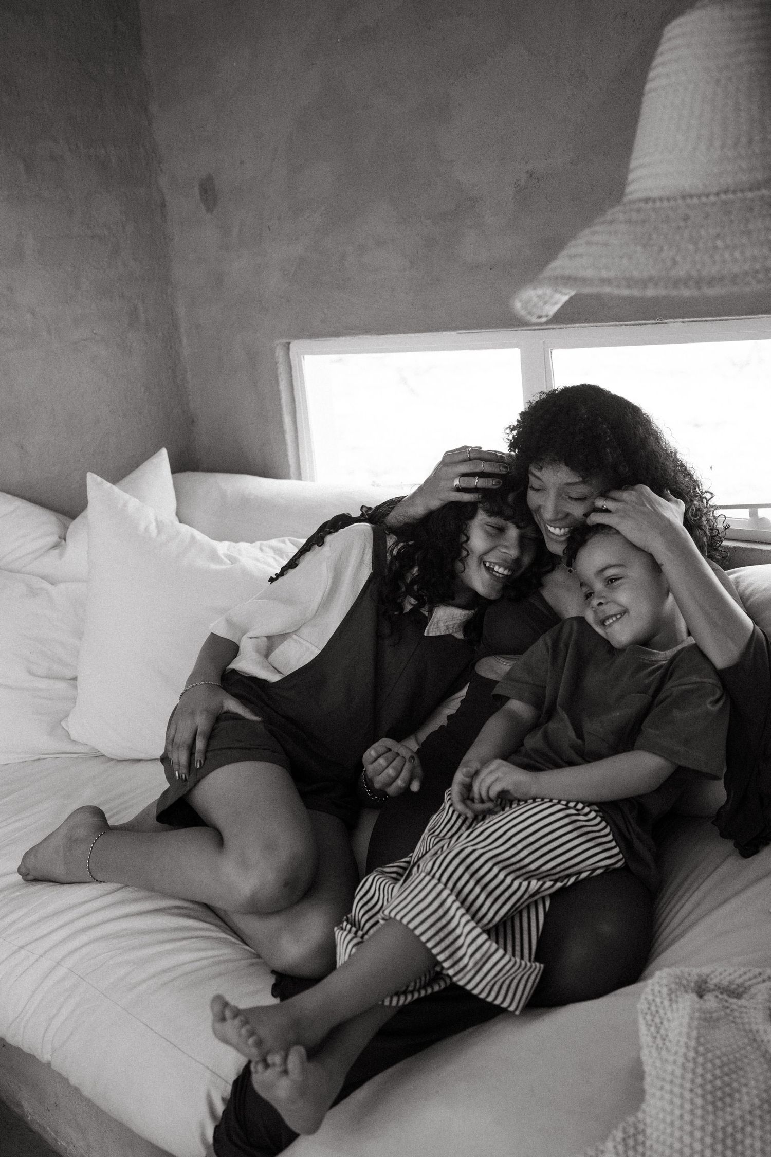 Candid black and white photo of family snuggling together on white bedding.