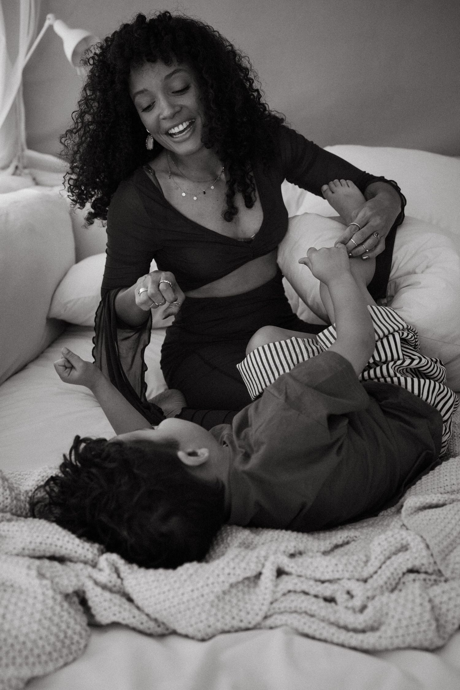 A tender black and white photo series showing playful moments between parent and child on a bed.