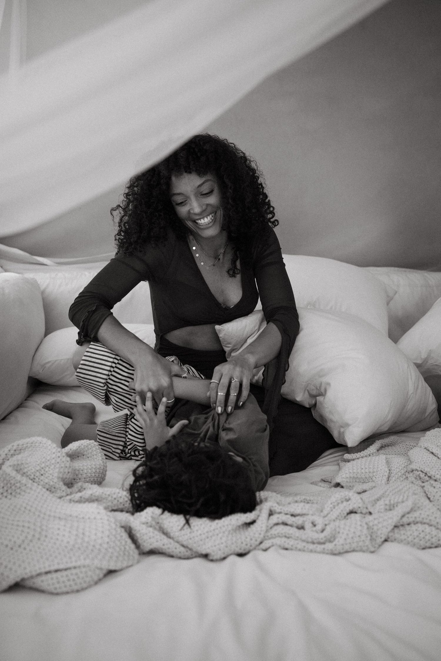 Black and white images capturing loving interactions between parent and child on cozy bedding.