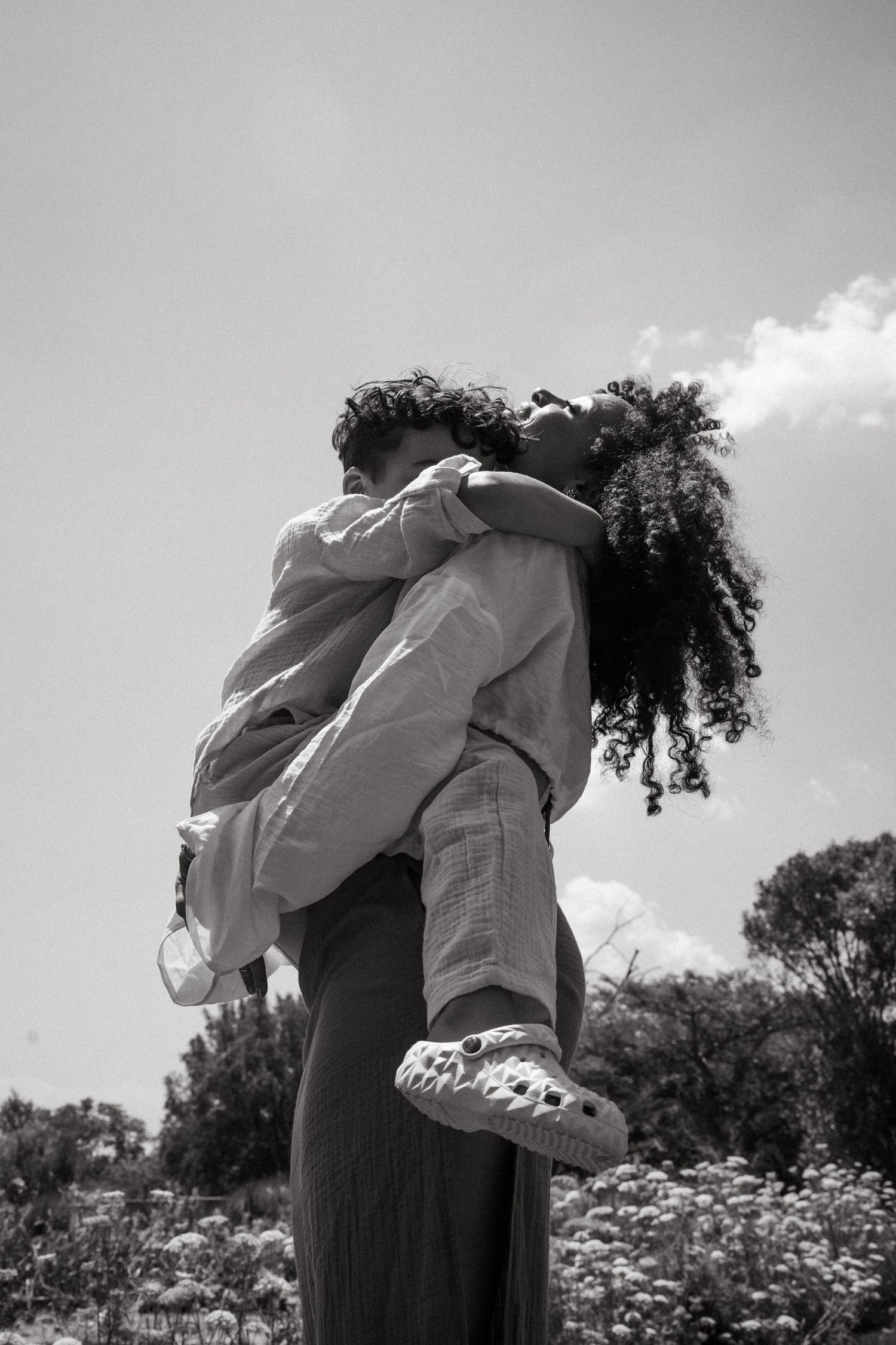 Black and white portrait of embrace in flowering meadow with dramatic lighting.