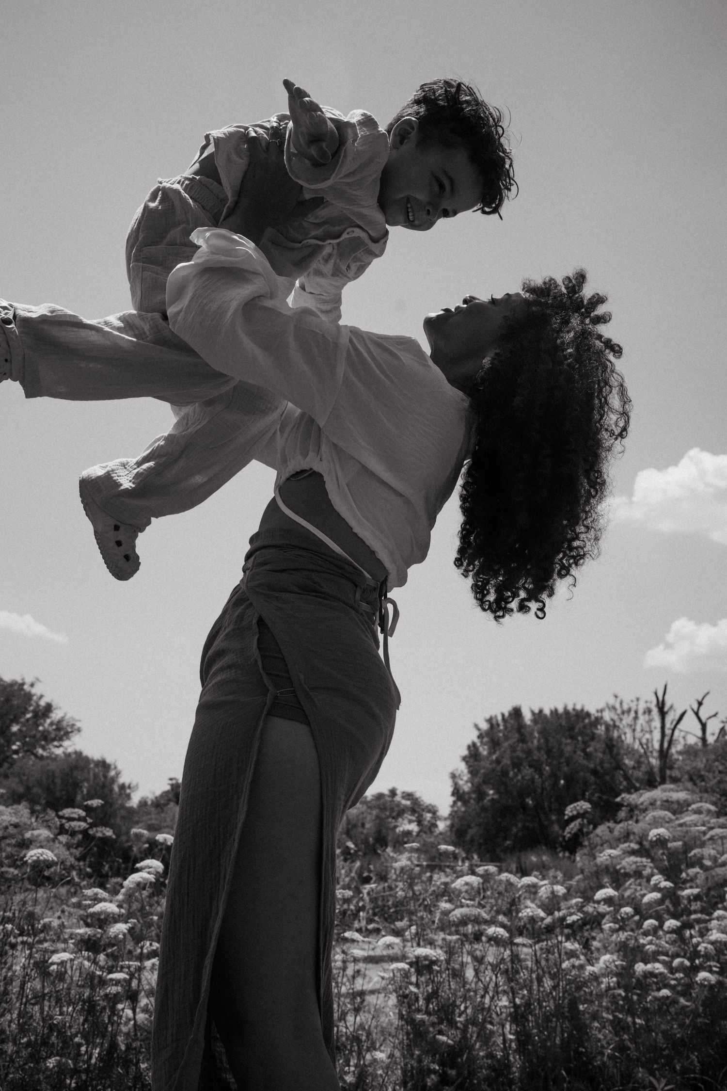 Black and white artistic photo of a figure leaping joyfully in a field of wildflowers on a sunny day.