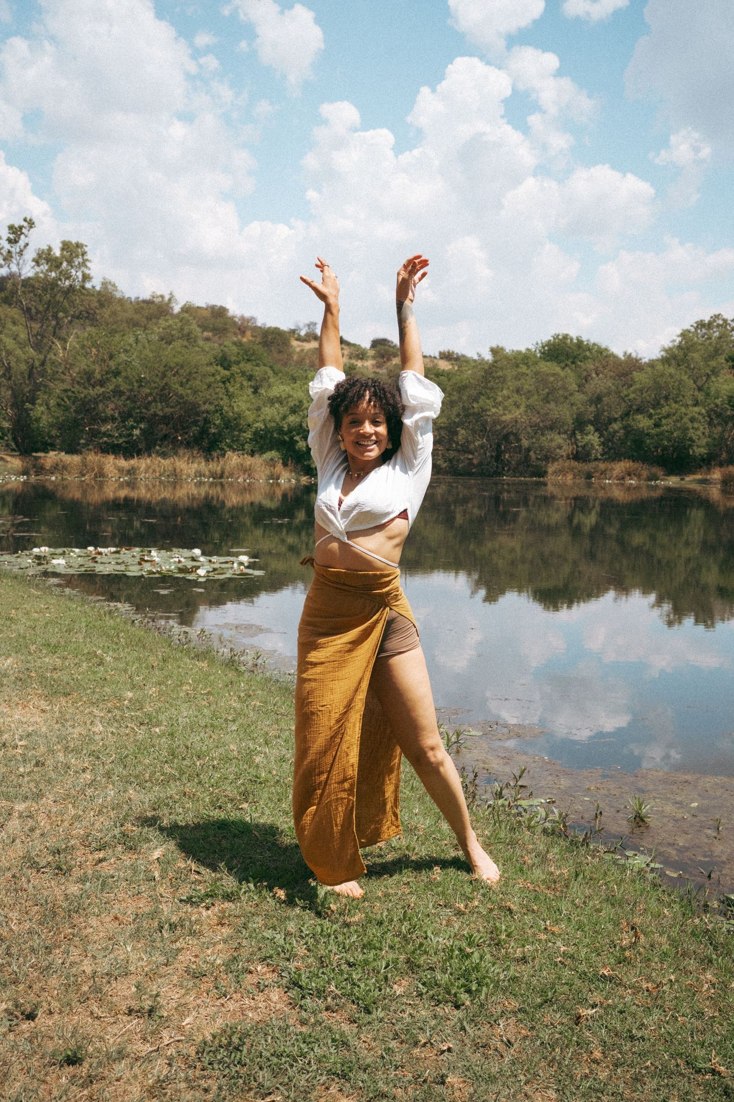 Joyful dance-like poses captured by a lake on a bright cloudy day.