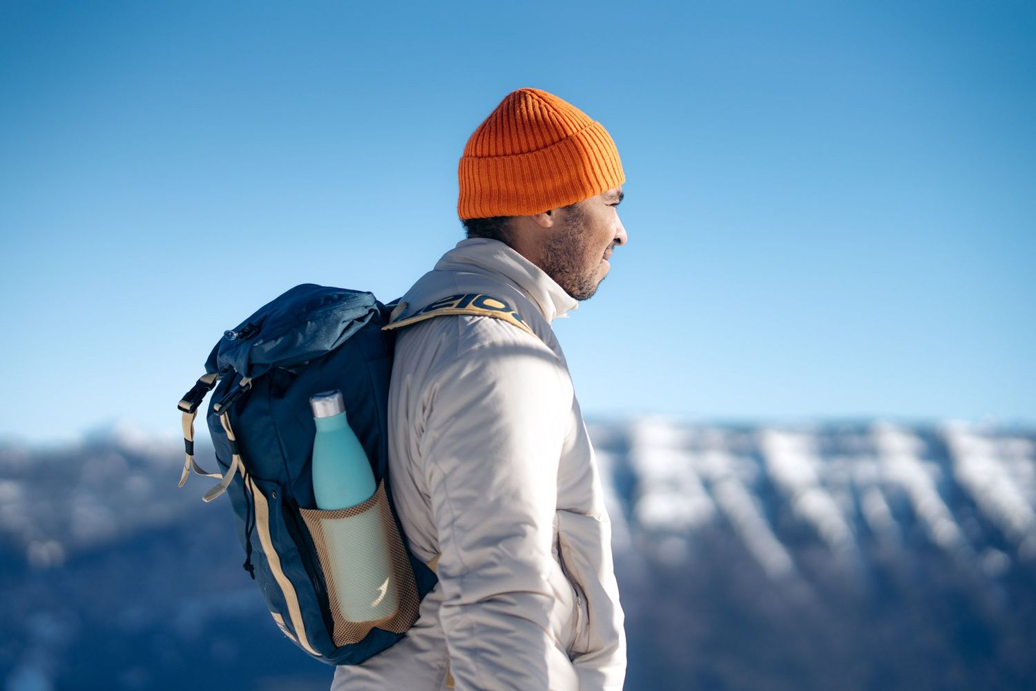 Un randonneur avec un bonnet orange et un sac à dos est debout devant les sommets enneigés de chartreuse lors d'une randonnée en raquettes